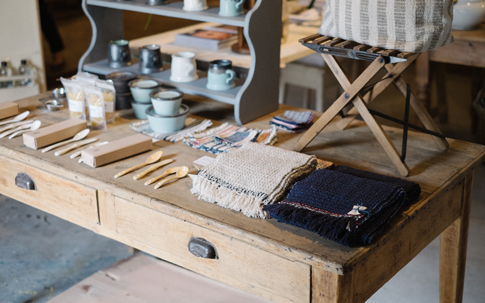 左のカトラリーと器は、鹿児島県の「ONE KILN」のもの。右手前にあるのは、福岡を拠点にオーガニックコットンや手紬の糸を使って、ガラ紡績機で織る「Suno & Morruson」のストールとウーブルオリジナルのコースターなど。 